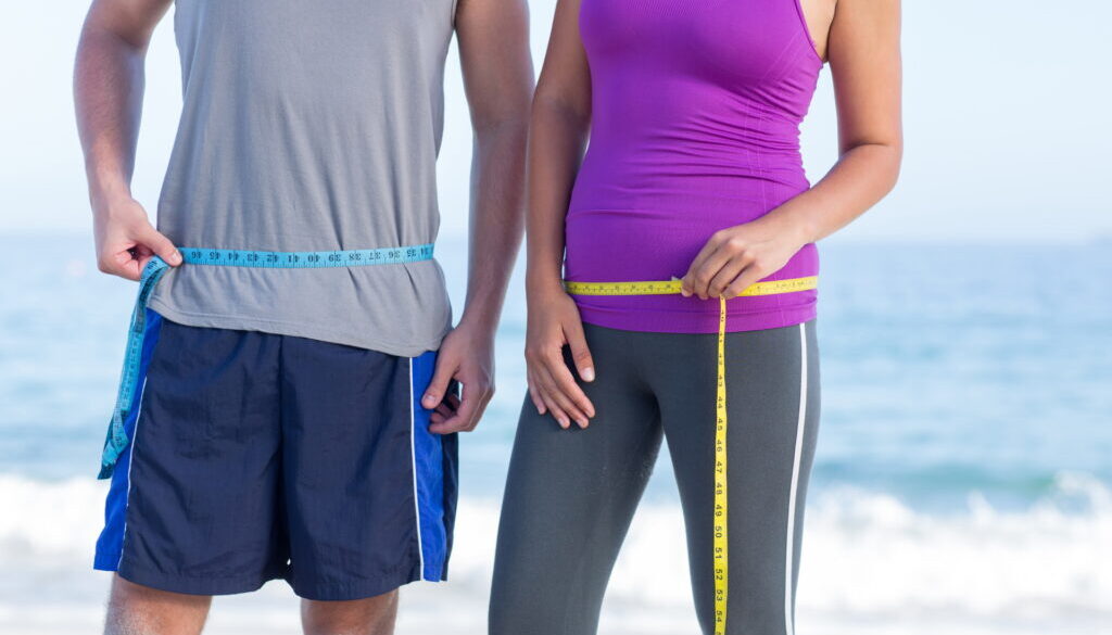 Couple measuring their waist at the beach