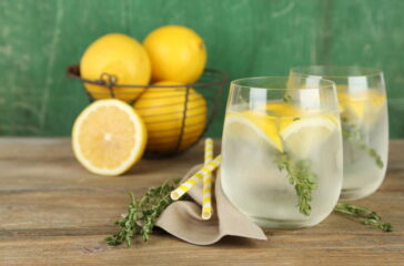 Tasty cool beverage with lemon and thyme, on wooden background